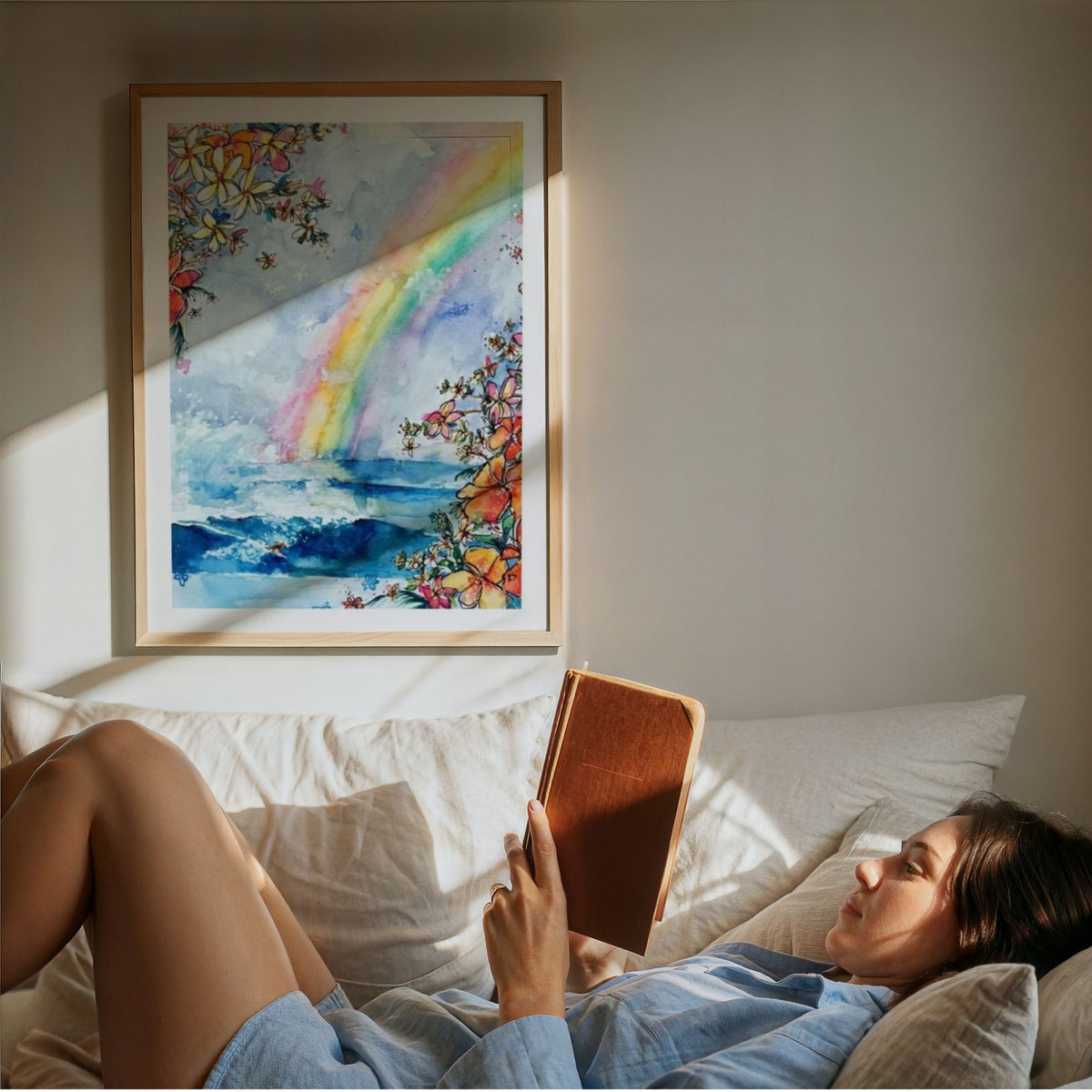 Wave Under the Rainbow watercolour surf art print by Rebekah Steen framed beside someone reading a book