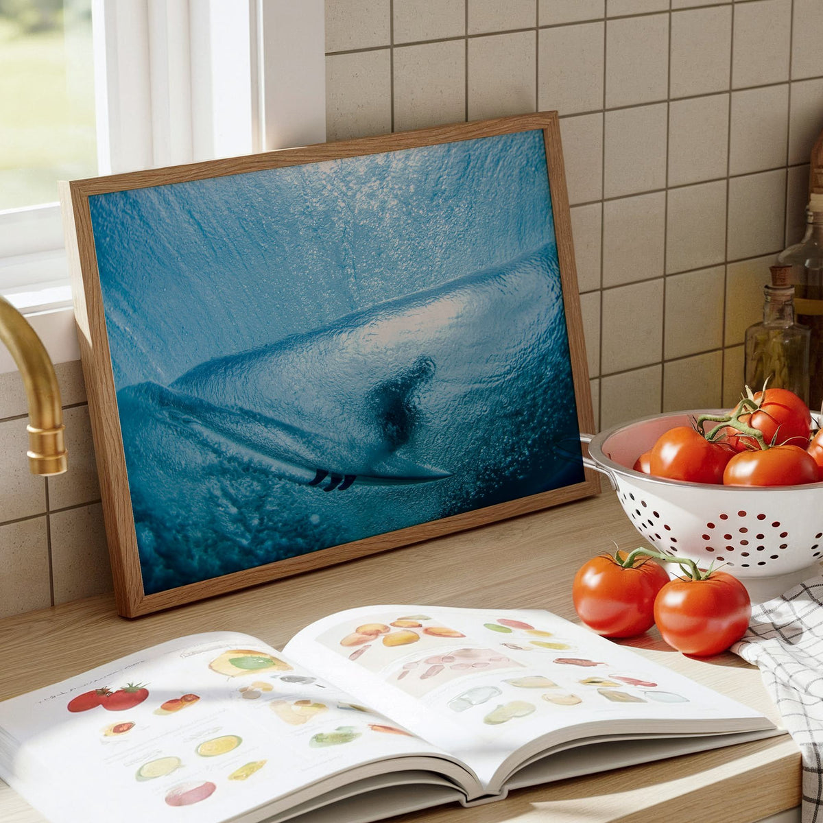 Aqua Cocoon surf photography print by Sean Davey framed and leaning on a kitchen counter beside tomatoes and a cookbook