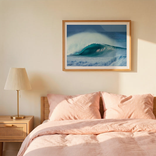 Aqua Plume surf photography print with a white border by Sean Davey framed above a bed with pink bedding