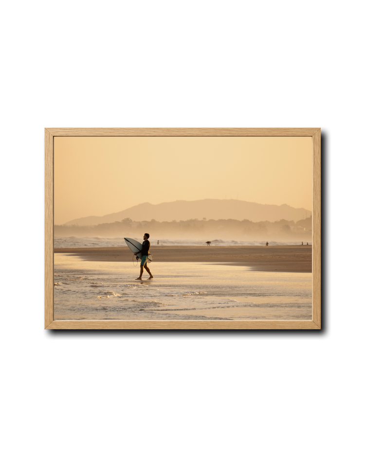 Framed QUIVER photograph of a surfer walking along a beach at sunrise