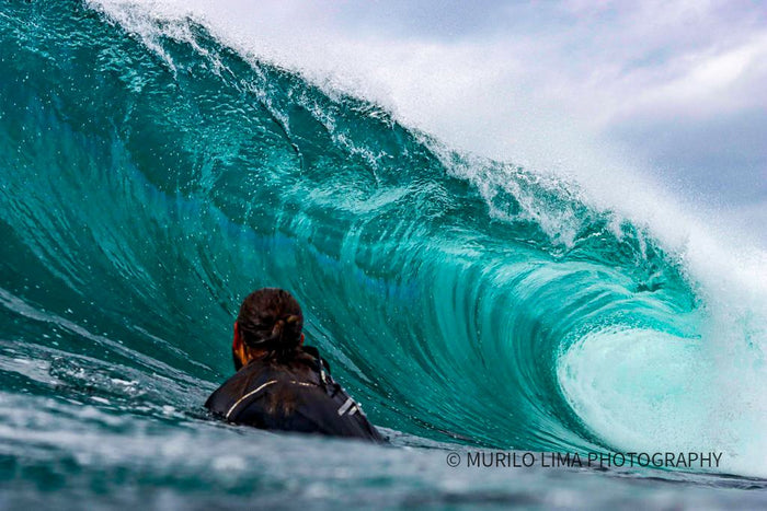 Surfer in the water watching a turquoise barrel break, photographed by Murilo Lima