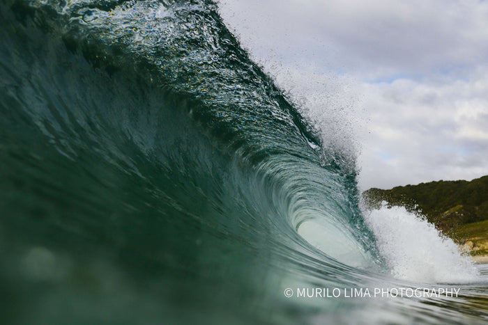 Green barrel peeling towards a wooded headland, in-water photograph by Murilo Lima