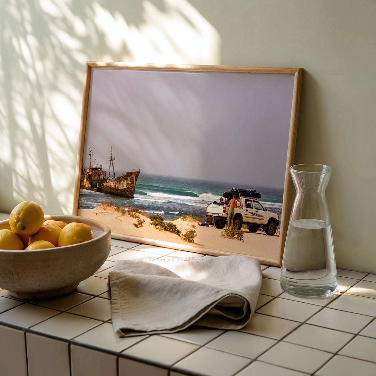 Shipwrecks surf photography print by John Seaton Callahan framed and leaning on a tiled kitchen counter beside lemons